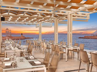 Open restaurant area with sea and harbor view at sunset.