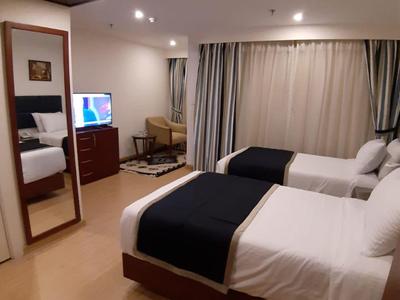Hotel room with two single beds, bedside table, chair, mirror, and curtains.
