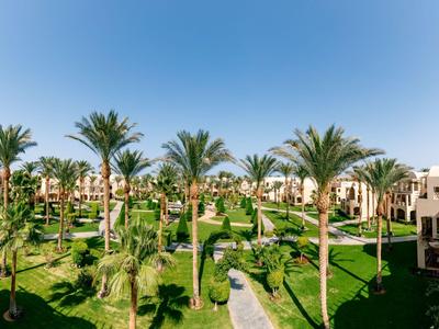Vista de un resort con palmeras, césped verde y edificios de varios pisos bajo un cielo despejado.