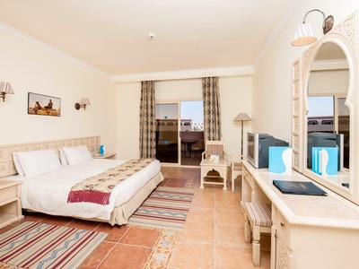 Helles Hotelzimmer mit Doppelbett, Teppichen und Balkon mit Blick nach draußen.