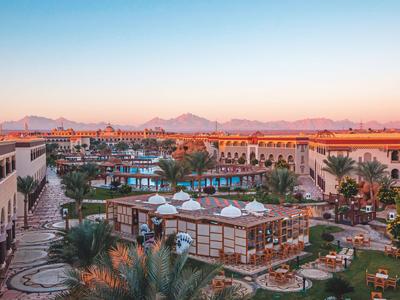 Amplio resort con piscina, pabellones y palmeras al atardecer en una zona desértica.