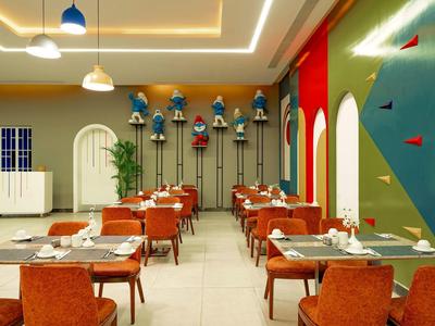 Moderner Gastraum mit orangen Stühlen, blauen Pendelleuchten und einer Kletterwand an der grünen Wand.