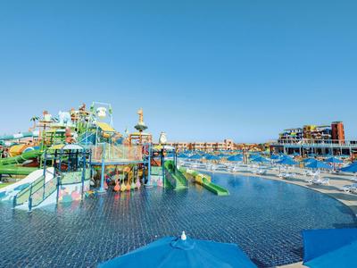 Groot waterpark met glijbanen en ligstoelen onder een heldere blauwe lucht.