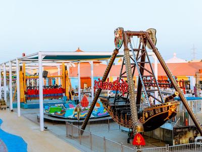 Parco divertimenti con una grande nave pirata come attrazione principale accanto a giostre colorate.