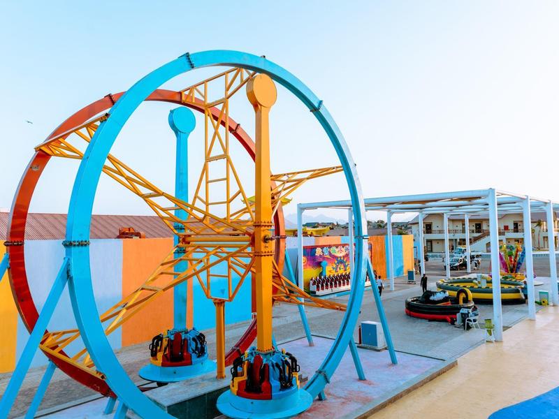 Bunter Spielplatz mit blauem Rundfahrgeschäft und Autoscooter unter blauem Himmel.