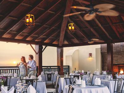 Offener Speisesaal mit gedeckten Tischen und Paar bei Sonnenuntergang auf der Terrasse.