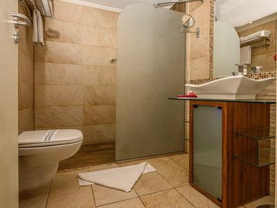 Lichte badkamer met beige betegelde muren, toilet, douche met matglazen scheidingswand en wastafel