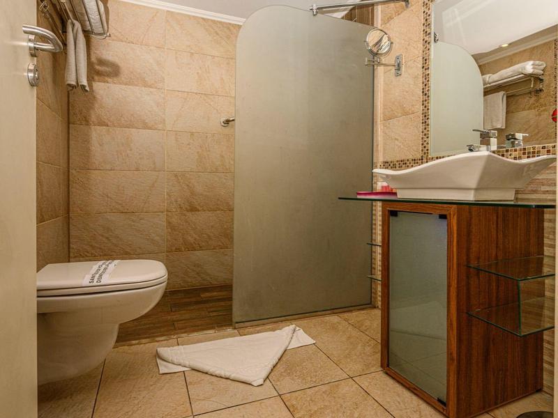 Baño moderno con azulejos marrones, ducha con vidrio esmerilado, lavabo y inodoro.