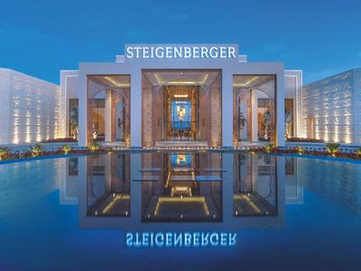 Modernes Hotel mit symmetrischem Eingangsbereich und großem reflektierendem Wasserbecken bei Nacht.