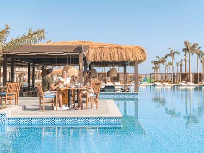 Entspannter Poolbereich mit Bar, Sonnenliegen und Palmen unter klarem Himmel