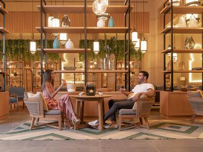 Zwei Personen sitzen in einer eleganten Hotellobby mit moderner Beleuchtung und Regalen.