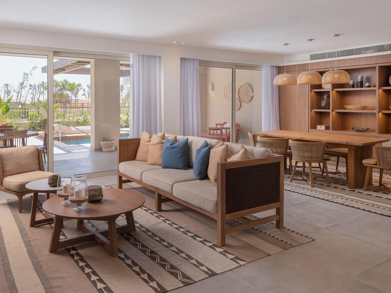 Helles Wohnzimmer mit beigem Sofa, Holztischen, Teppichen und angrenzendem Essbereich mit Holzmöbeln.