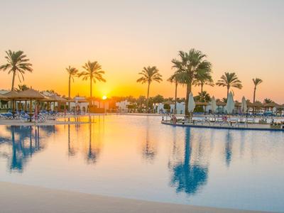 Atardecer sobre una piscina tranquila con palmeras en un resort hotelero.
