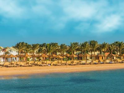 Hotelový resort s palmami a písečnou pláží u klidného modrého moře pod oblačnou oblohou