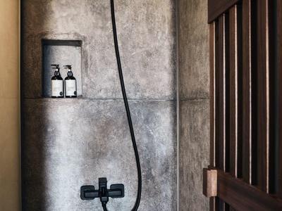 Dunkle, minimalistische Dusche mit grauen Fliesen, schwarzem Duschkopf und zwei Flaschen auf Ablage.
