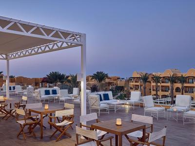 Offene Terrasse mit Sitzgelegenheiten und Tischen in einem Hotel bei Sonnenuntergang.