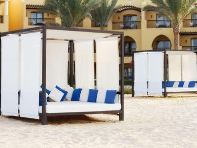 Cabanes blanches avec coussins bleus sur une plage devant un hôtel.