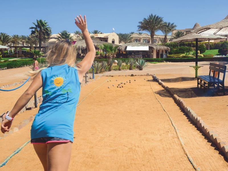 Personne lançant une boule dans un terrain de pétanque en plein air sous le soleil.