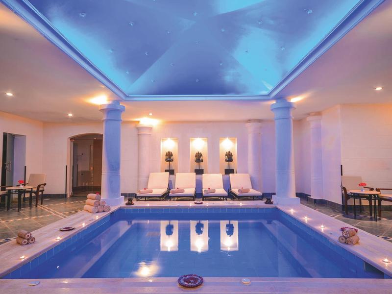 Piscine intérieure avec éclairage bleu et chaises longues dans un espace équipé pour la détente.