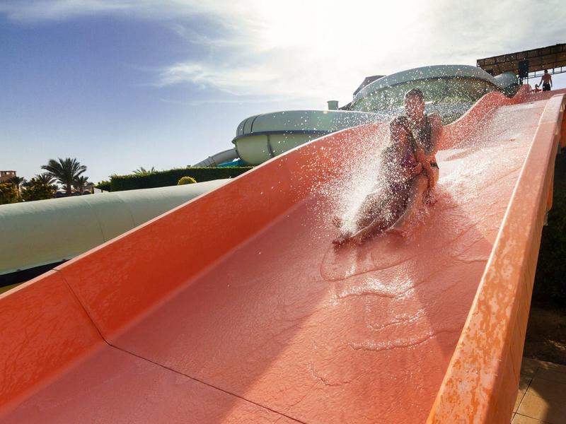 Personne glissant sur un toboggan orange dans un parc aquatique ensoleillé.
