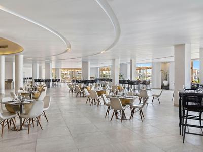 Large, modern hotel restaurant area with many tables and chairs, minimalist design.