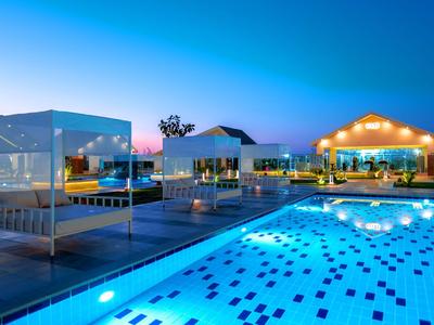 Modern illuminated pool area with loungers and pavilions at a hotel at night.
