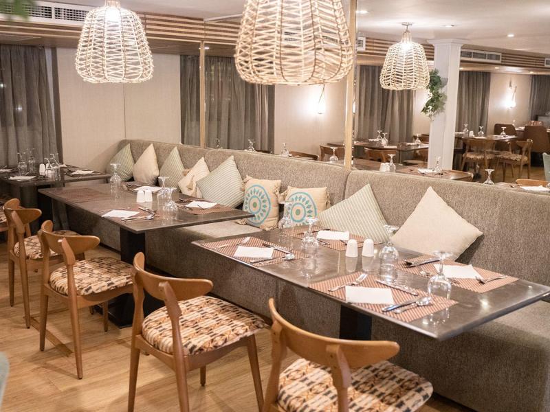 Salle à manger d'hôtel avec tables, chaises en bois et grandes banquettes beiges.