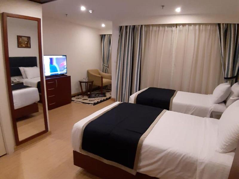 Zweibettzimmer mit weißen Bettdecken, schwarzen Decken, großem Spiegel und Holzfußboden.