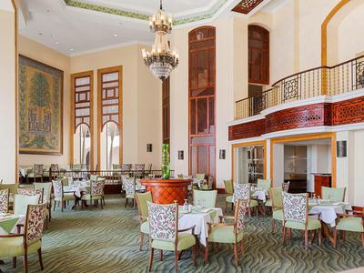 Elegant hotel dining area with chandeliers, patterned chairs, and large windows letting in natural light.
