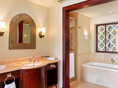 Elegant bathroom with wooden vanity, arch mirror, wall sconces, and a bathtub with decorative window.