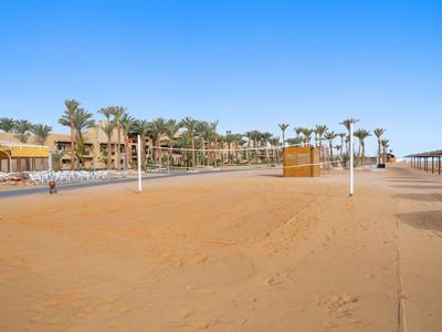 Pusta piaszczysta plaża z siatką do siatkówki i budynkami hotelowymi w tle pod czystym niebem.