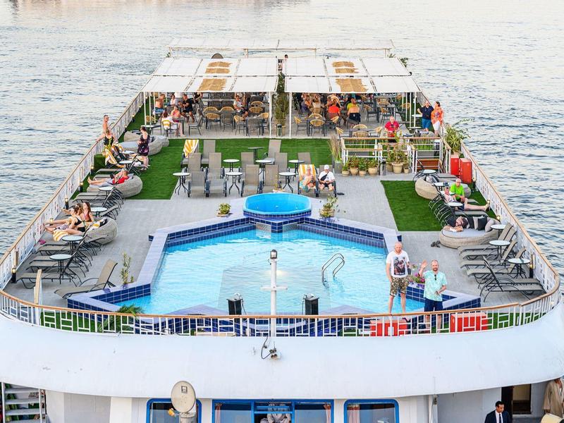 Top deck of a cruise ship with a swimming pool and sun loungers by the water.