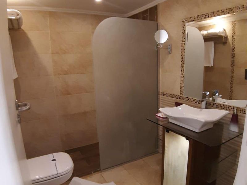 Modern hotel bathroom with toilet, sink, mirror, and glass shower partition.