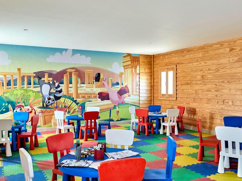 Salle de jeux colorée pour enfants avec tables, chaises et mur en bois.