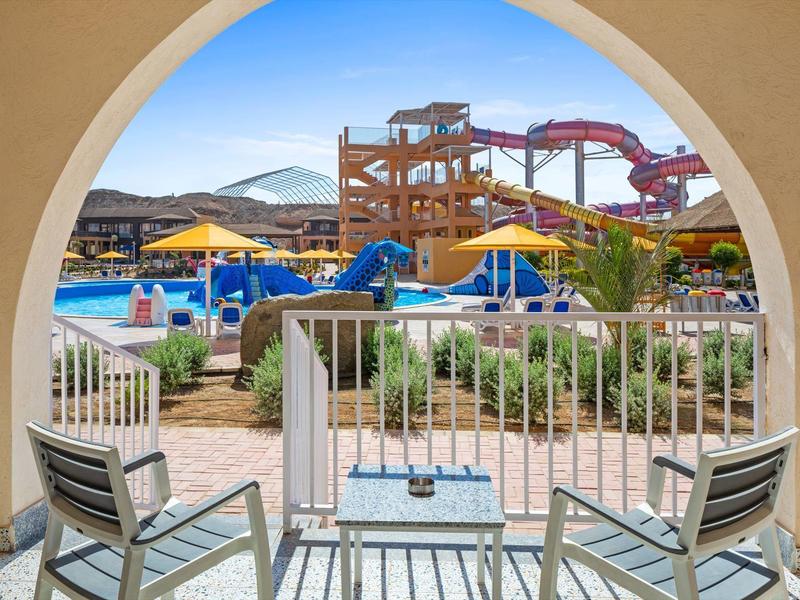 Vista su un parco acquatico colorato con scivoli dall'arco di una terrazza con sedie e tavolo.