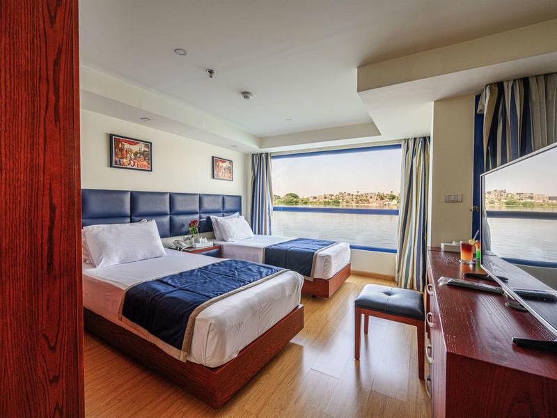 Hotelkamer met twee bedden, groot raam met uitzicht op water, bureau en tv.