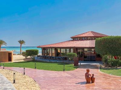 Gebouw met rood dak en terras aan zee met palmbomen en blauwe lucht