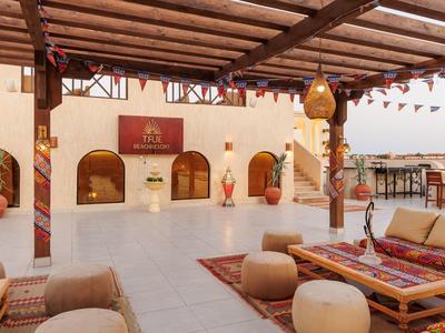 Cozy outdoor lounge area with carpets, cushions, and wooden pergola at a desert hotel.