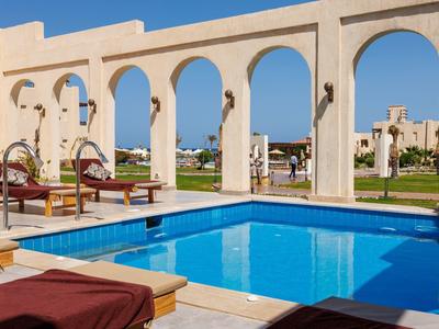 Outdoor pool with lounge chairs under white arches in sunny resort area.