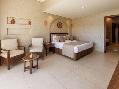 Spacious hotel room with a large bed, two chairs, side table, and neutral decor.