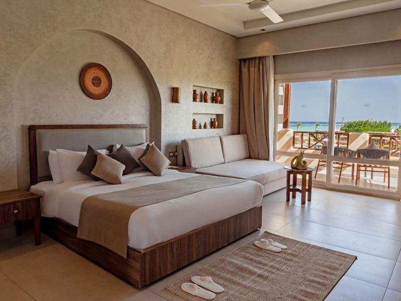 Spacious hotel room with king bed, sofa, terrace, and sea view.