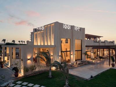 Hôtel moderne aux fenêtres chaleureusement éclairées au coucher du soleil avec des palmiers au premier plan.