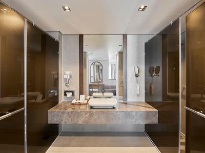 Salle de bain moderne avec plan de travail en marbre, lavabo mural, grand miroir et armoires brillantes foncées.