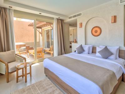 Chambre d'hôtel lumineuse avec grand lit, tons neutres et portes coulissantes vers terrasse extérieure.