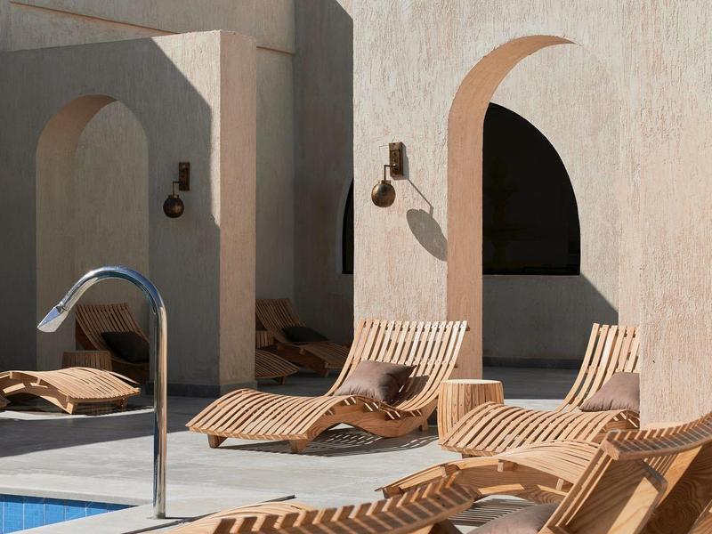 Bord de piscine ensoleillé avec chaises longues rayées et murs beiges avec arches.