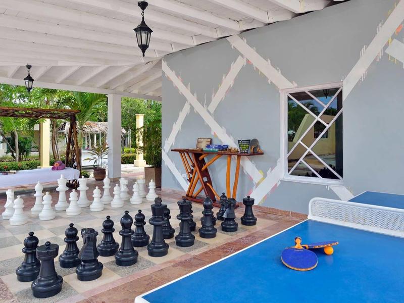 Venkovní terasa s velkými šachy a modrým pingpongovým stolem pod bílou střechou.