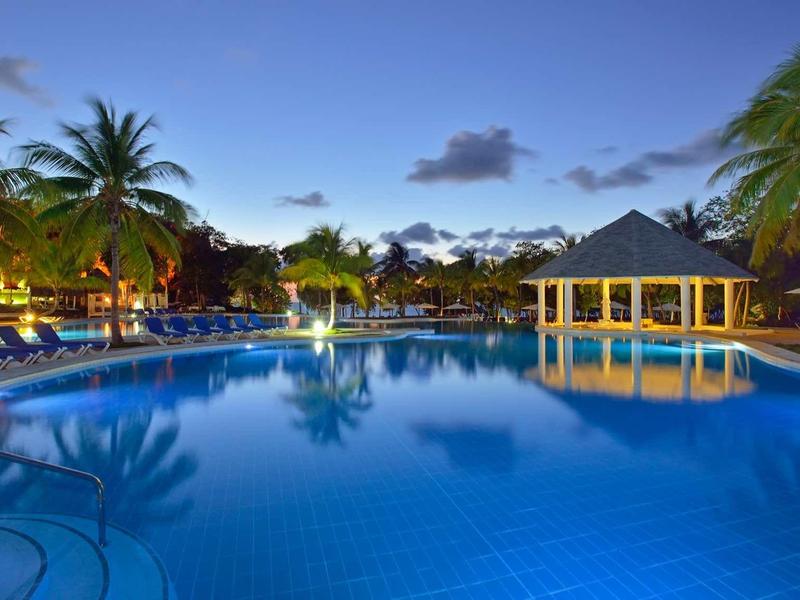 Noční osvětlený bazén s palmami a altánkem v tropickém prostředí.