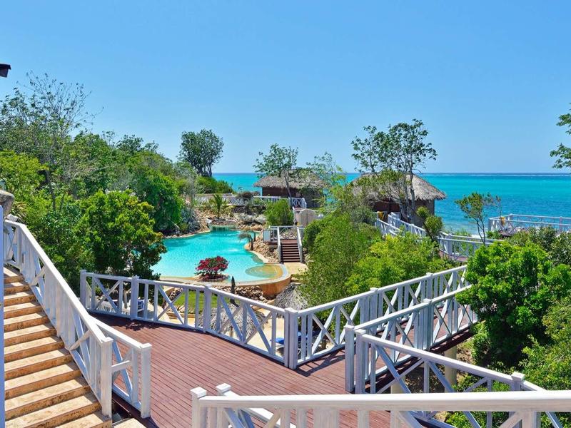 Bazén s výhledem na moře, obklopený zelení a dřevěnými terasami.