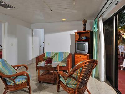 Wohnzimmer mit Rattanstühlen, Glas-Couchtisch, Fernseher und offenem Zugang zur Terrasse bei Abendlicht.