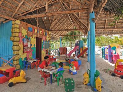 Kinder spielen in einem bunten, überdachten Außenbereich mit Spielzeug und Rutschgeräten.